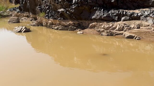 Panning shot from a muddy wadi to a dry, rocky desert landscape in Saudi Arabia.