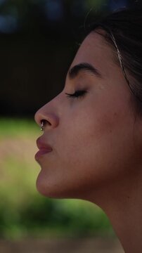 Vertical close-up side profile of a young Iranian woman practicing slow breathing meditation outdoors with eyes closed, capturing mindfulness, calm, relaxation and mental wellness.