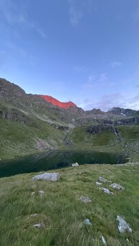 Alpine mountain lake surrounded by green meadows and rocky peaks illuminated by red alpenglow in the Schladming Tauern near G&ouml;riach, Austria.
