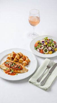 Fish dish with Romesco sauce, patatas bravas, seafood salad, and a glass of ros&eacute; wine