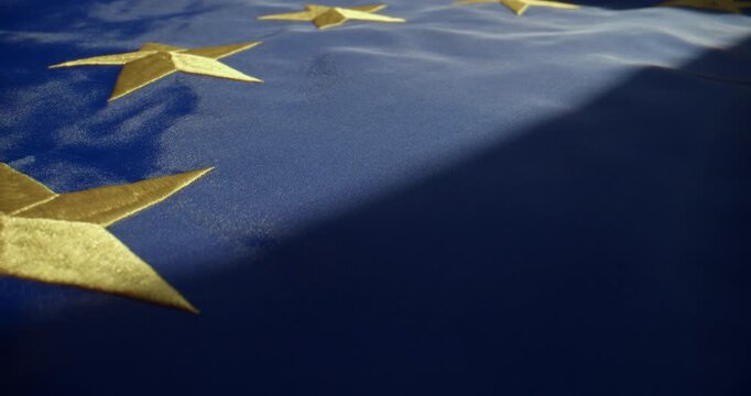 Closeup cinematic shot of the European Union flag lying on a horizontal surface under directional local light. Slow push-in camera movement captured with a probe lens and slider.