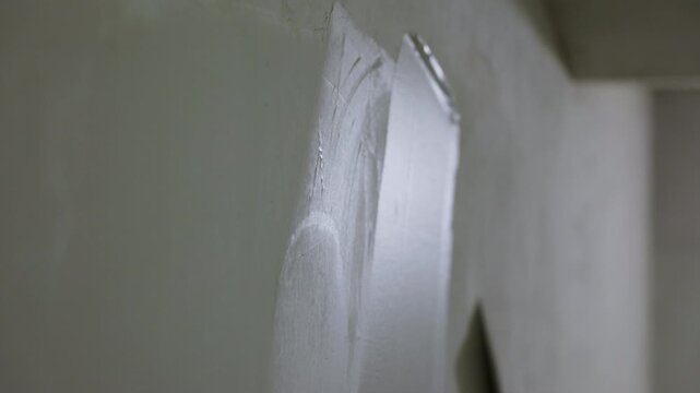 Worker smoothing plaster on interior wall with wide putty knife