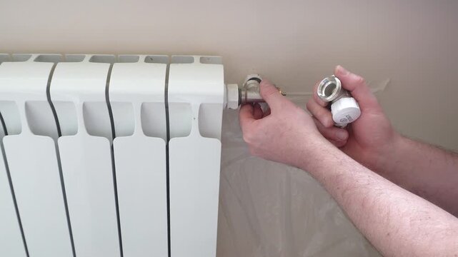 Installing a thermal head on a radiator. A man installs a control valve with a thermal head on a white sectional battery. The video demonstrates the installation process of heating equipment.
