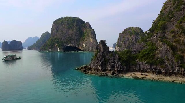 Serenity of Ha Long Bay: A wider daytime orbital tracking drone shot of a luxury yacht navigating emerald waters among majestic karst mountains in Vietnam