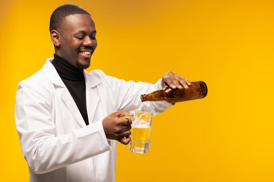 Man in white coat joyfully pouring beer from a bottle into a glass against yellow background