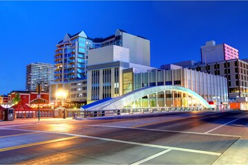 Fototapeta premium Reno, Nevada downtown at dusk, featuring illuminated buildings, a modern arched bridge, city streets, and vibrant blue evening skies.