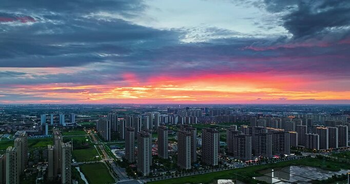 Dramatic orange and purple clouds glow over a modern residential cityscape during a vibrant sunset in evening light.