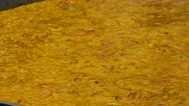 Close-up view of rice with saffron and seafood simmering in large flat pan during a traditional Spanish paella cooking competition. Hot broth bubbling and boiling over low fire, creating rich texture