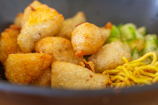 Indonesian fried fish cake pempek served in a bowl with yellow noodles and sliced cucumber
