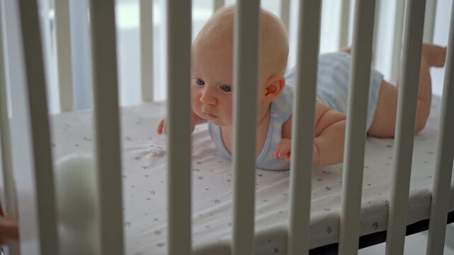 Close-up of father placing baby monitor camera in front of five-month-old son in crib. Infant care.