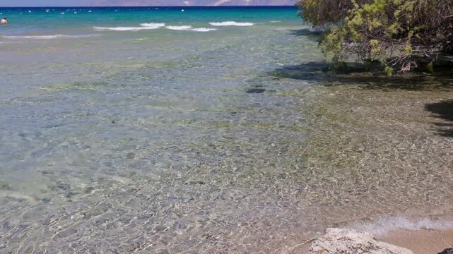 Shallow clear water rippling over sandy seabed at Almyros beach near Agios Nikolaos in Crete, Greece, distant mountains over blue sea
