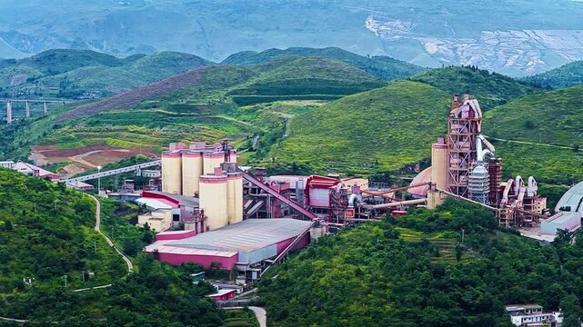 High angle shot of a large modern industrial factory facility nestled among lush green mountain hills during daytime.