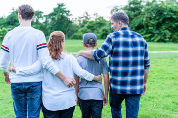 Fototapeta premium Back view of a multiracial family of four walking together in a green park