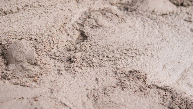 Wet muddy soil texture with rough clumps, earthy neutral tones, shallow focus, and natural abstract surface detail suitable for background, design, construction, weather, and outdoor environment.