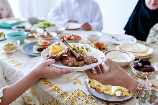 Hands serving grilled meat at a family dinner table with diverse guests