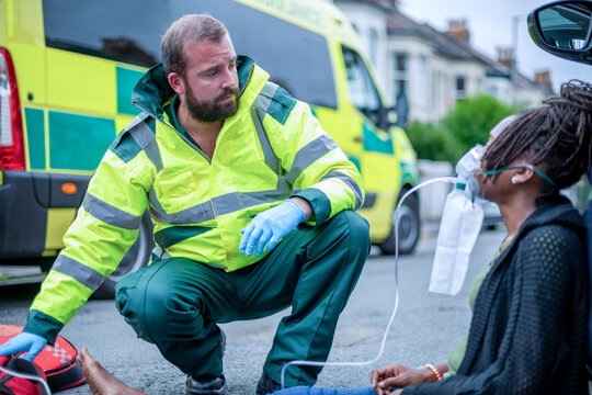 White male paramedic assisting an injured Black woman beside an ambulance