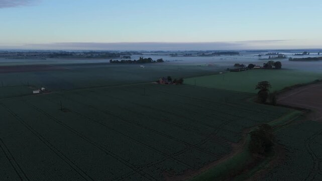 Mist drifts low over green fields at dawn
