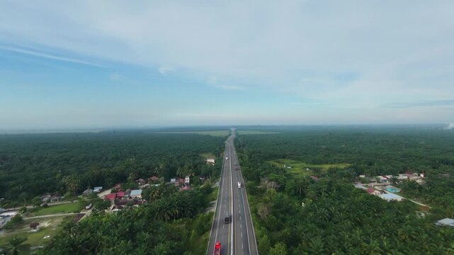 aerial view of a rural village road intersecting beneath a toll road overpass, surrounded by extensive palm oil plantations and tropical countryside.