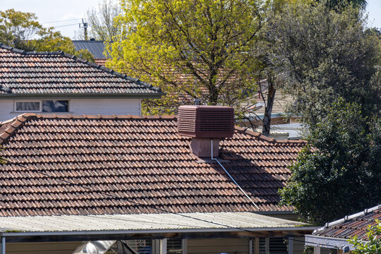 A terracotta tiled roof on a suburban Australian house, featuring an evaporative air cooling unit, framed by trees and neighbouring roofs. Home energy efficiency, residential climate control