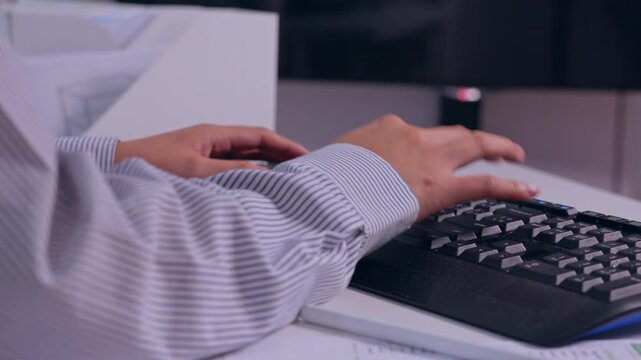 Office worker typing on computer keyboard at desk, hands and arm near paperwork, striped shirt sleeves, focused digital work posture in modern workspace setup