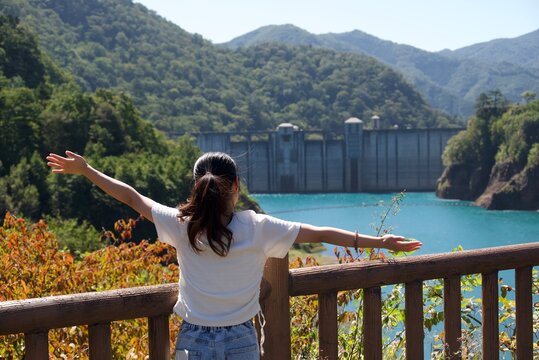 四万川ダムと奥四万湖の絶景に向かって両手を広げる女性の後ろ姿 Woman spreading arms toward scenic view of Shima River Dam and Okushima Lake