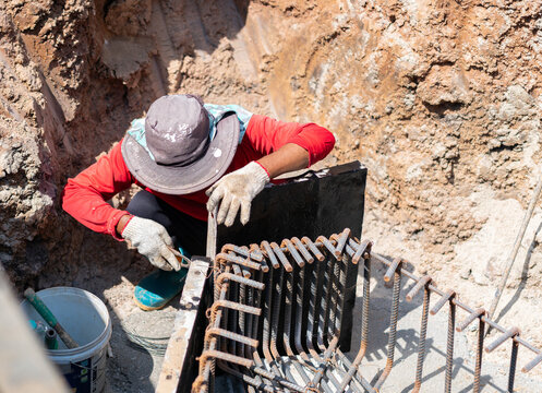Builder preparing steel reinforcement cage and formwork in a soil excavation pit at a construction site.