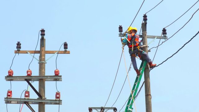 Electrician works on tall pole. He wears bright safety gear. Ladder leans against the pole. Sky is clear and blue. He focuses on his task. Image shows utility work in progress