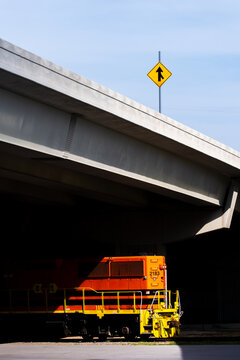 Orange locomotive parked beneath highway overpass with merge sign