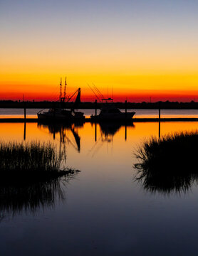 Fishing boats silhouetted at sunset in calm marsh harbor