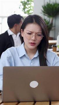 Stressed Asian Businesswoman Working on Laptop in Busy Coworking Office