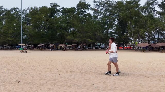 Young Couple Holding Drinks and Walking on Sandy Beach
