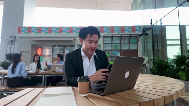 Smiling Asian Businessman Using Smartphone and Laptop at Outdoor Office