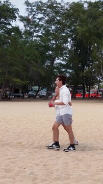 Young Asian Couple Walking on Sandy Beach Holding Drinks