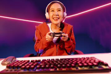 Host channel of smiling beautiful Asian girl streamer with joystick playing online game wearing headphones paste talking with viewers media online. Esport skilled team players in neon room. Stratagem. © InfiniteFlow