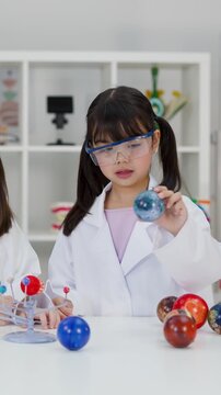 Young Girl in Lab Coat Studying Solar System Model in Science Class