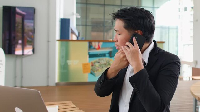 Stressed Asian Businessman Talking on Smartphone in Outdoor Coworking Space