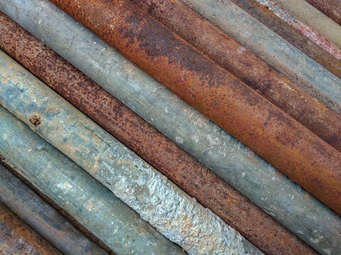 Rusty metal pipes aligned diagonally, showcasing various stages of corrosion