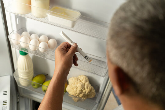 Man places an injection pen containing medication into home refrigerator next to food items. Concept of home-based treatment, medication storage, and use of drugs requiring refrigeration