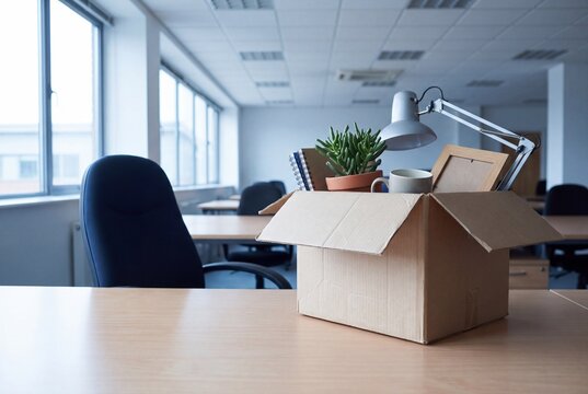 Box with personal belongings on empty office desk, layoff concept