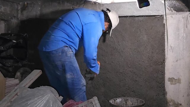 Bricklayer using a trowel to remove excess mortar from a wooden board