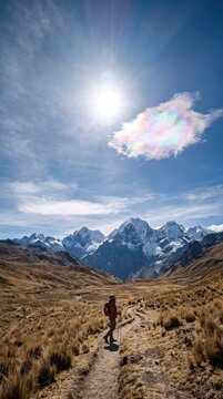 A lone tiny traveler standing in a vast high-altitude grassland in the Peruvian Andes, a small but vivid iridescent cloud glowing pastel pink, green and violet beside the sun, distant mountain ridges
