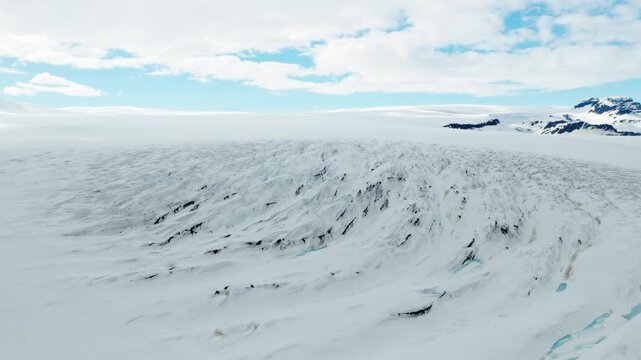 Vatnajokull ice cap covers a broad volcanic highland in southeast Iceland, with deeply incised glacial channels, exposed dark rock and snow covered ridges along the ice margin, drone forward flyover.
