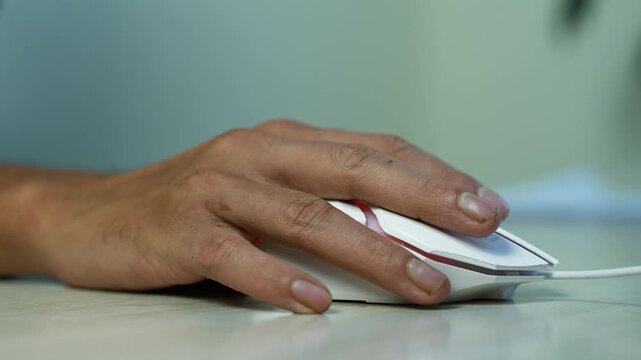Hand Using a Wired Computer Mouse on Desk, Close-up of a person's hand using a white wired computer mouse on a desk, showing everyday office work and technology use.