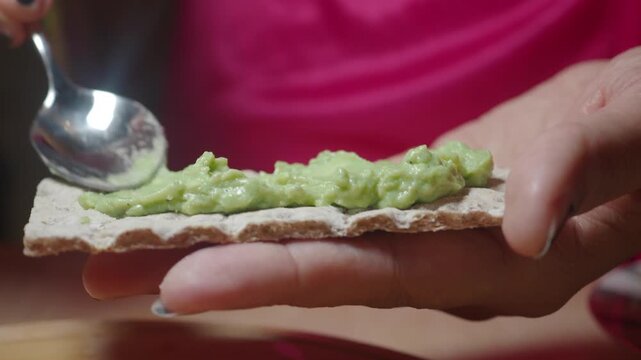 Woman's hands spreading green avocado spread on crispbread with a spoon close up shot.