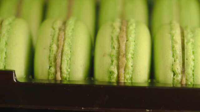 Close up motion of green macarons in dark plastic box, fresh baked pastry, sweet dessert, confectionary on display, delicious food.