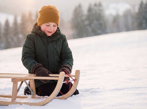 Junge macht Pause mit Holzschlitten am verschneiten Rodelhang