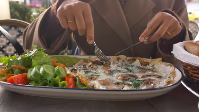 Close up video of a person enjoying a delicious mushroom omelet with a fresh salad, cutting and eating the meal at an outdoor cafe on a sunny day.