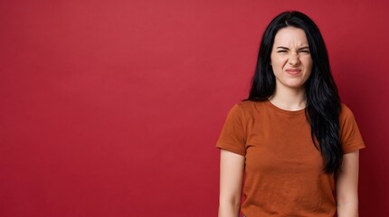 Fototapeta premium Portrait of a young woman with a disgusted facial expression wrinkling her nose against a red background with copy space