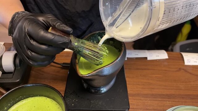 The preparation of matcha using a bamboo whisk shows vibrant green matcha being freshly whisked in a ceramic bowl on a wooden table.