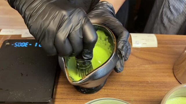 The preparation of matcha using a bamboo whisk shows vibrant green matcha being freshly whisked in a ceramic bowl on a wooden table.